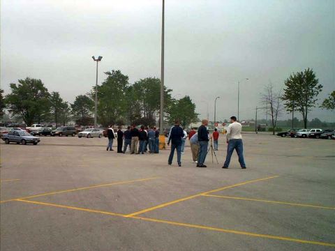 2000 Ford Crown Victoria - A group of people are standing in a parking lot, some with cameras, under an overcast sky.