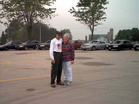 2000 Ford Crown Victoria - A couple stands in front of several parked Ford Crown Victorias, one of which is silver.