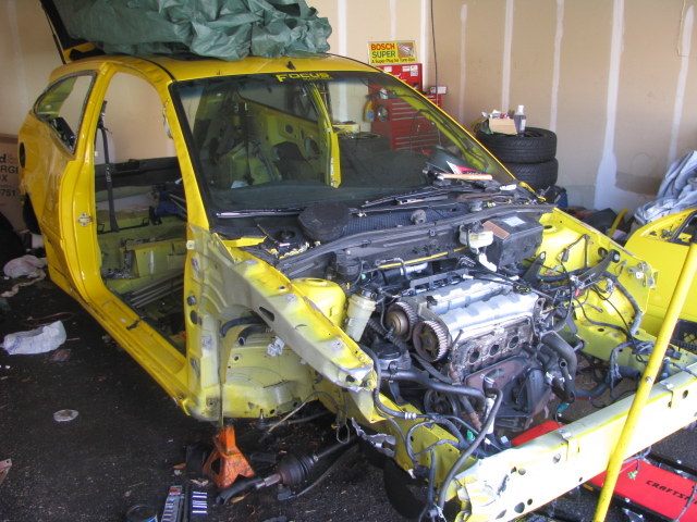 Yellow 2003 Ford Focus with doors and hood open, engine exposed, in a garage
