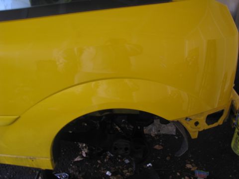 2003 Ford Focus - Rear quarter panel and wheel well of a yellow 2003 Ford Focus, showing the vehicle's body style.