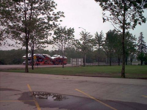 2000 Ford Crown Victoria - Car carrier truck transports multiple vehicles on a highway rest stop.