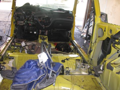 2003 Ford Focus - The interior of a yellow car has been stripped down, revealing exposed wiring and the bare metal frame.