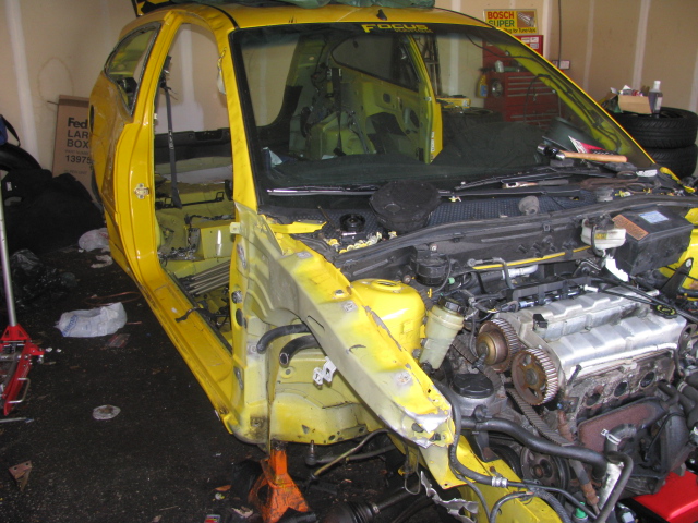Yellow Ford Focus torn down in a garage with fenders and doors off and engine exposed