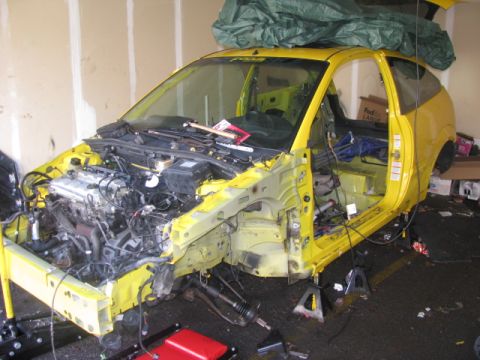 2003 Ford Focus - This yellow car is in a state of disassembly, with its engine exposed and interior stripped bare.