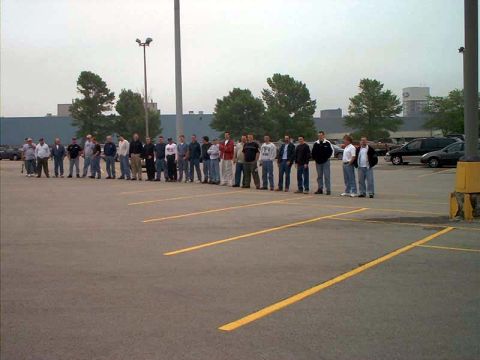 2000 Ford Crown Victoria - A group of men stand in a parking lot, with several vehicles visible in the background.
