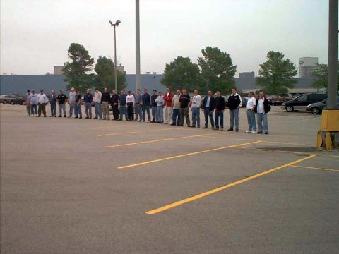 2000 Ford Crown Victoria - A group of men stand in a parking lot, with several vehicles visible in the background.