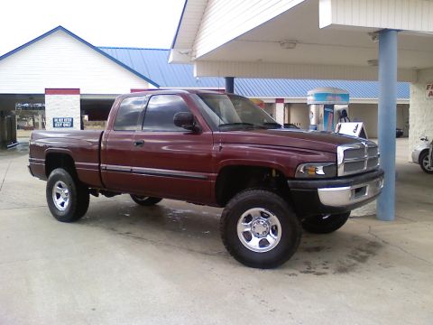 2001 Dodge 1500 - A maroon 2001 Dodge 1500 pickup truck is parked outside a building with a blue roof and white siding.