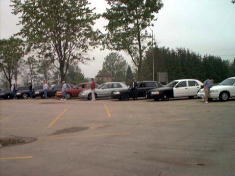 2000 Ford Crown Victoria - A line of police vehicles, including a Ford Crown Victoria, are parked in an outdoor lot under an overcast sky.