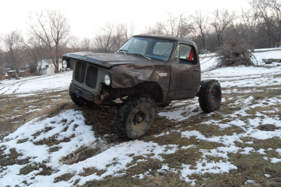 Brown Dodge pickup truck with damaged front end and large off-road tires, parked on a snowy hill