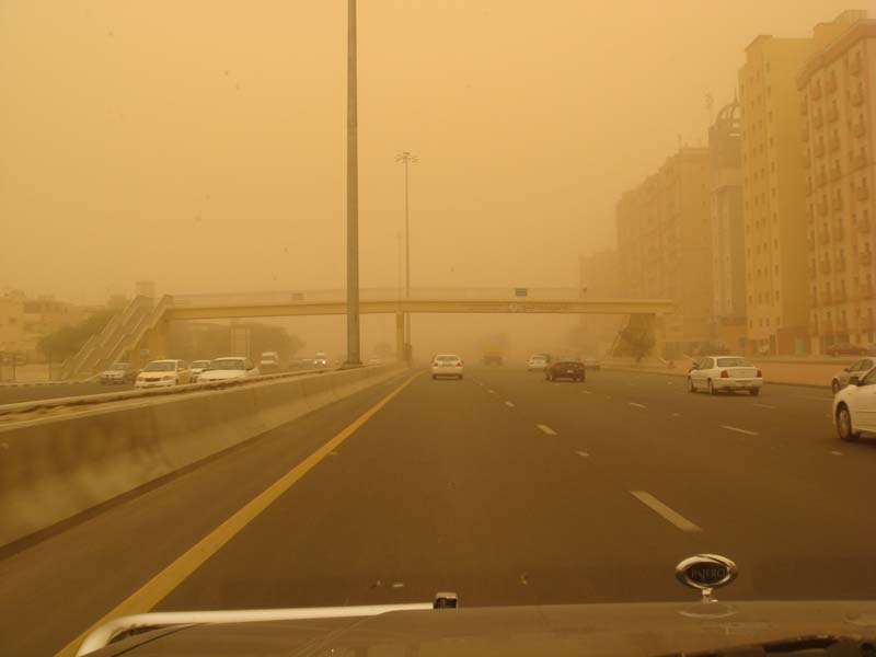 Highway traffic obscured by a sandstorm, with buildings visible in the distance