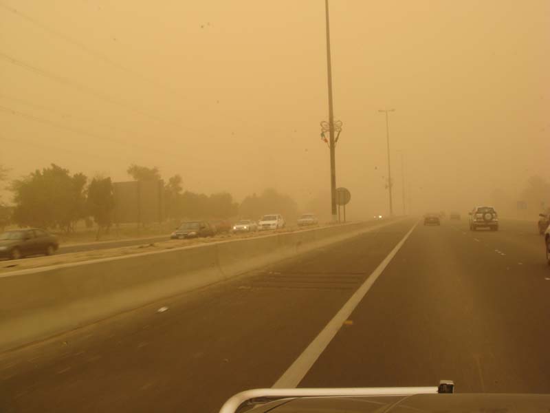 Highway traffic obscured by a sandstorm, with multiple cars visible on the road and a watermark at the bottom
