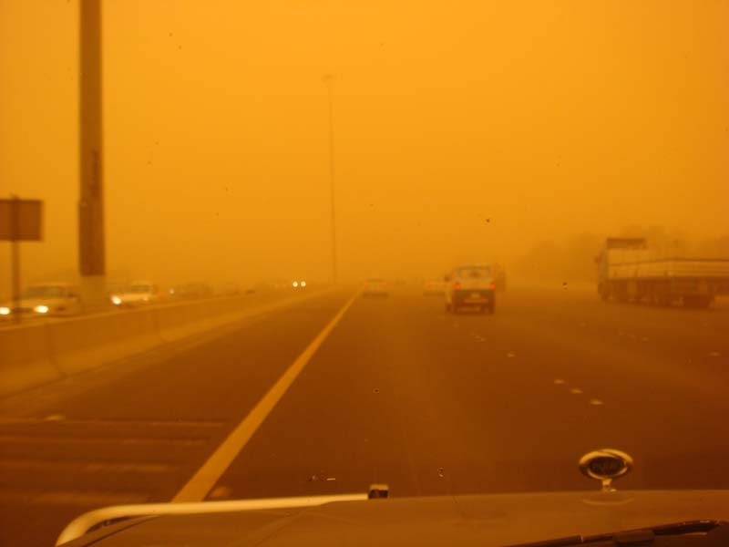 Highway driving in heavy orange sandstorm with limited visibility, multiple vehicles visible