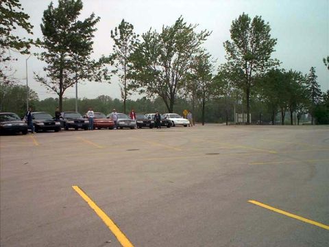 2000 Ford Crown Victoria - A group of sedans are parked in an outdoor lot under a cloudy sky.