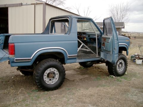 1984 Ford Bronco - Modified blue pickup truck with roll cage and large tires, parked outdoors. The vehicle appears to be a Ford Bronco from the early 1980s.