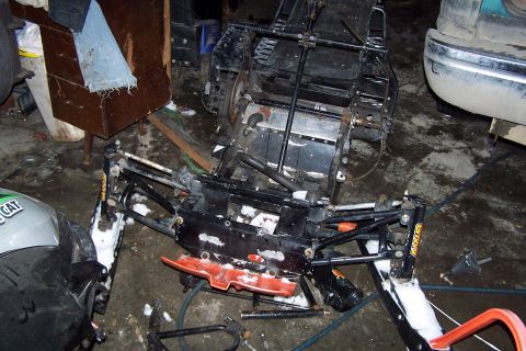 2004 Arctic Cat F-7 Firecat - Disassembled snowmobile chassis and front suspension components are laid out on a garage floor.
