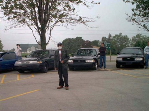 2000 Ford Crown Victoria - Multiple black Ford Crown Victorias are parked in a lot under a cloudy sky.