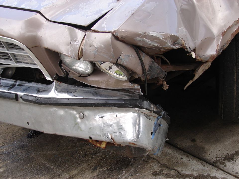 Crushed tan front fender, headlights and buckled chrome bumper after collision