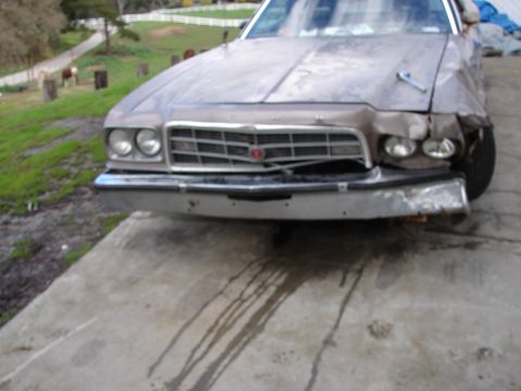 1973 Ford Ranchero - The front of a damaged vehicle sits on a concrete surface with fluid stains.