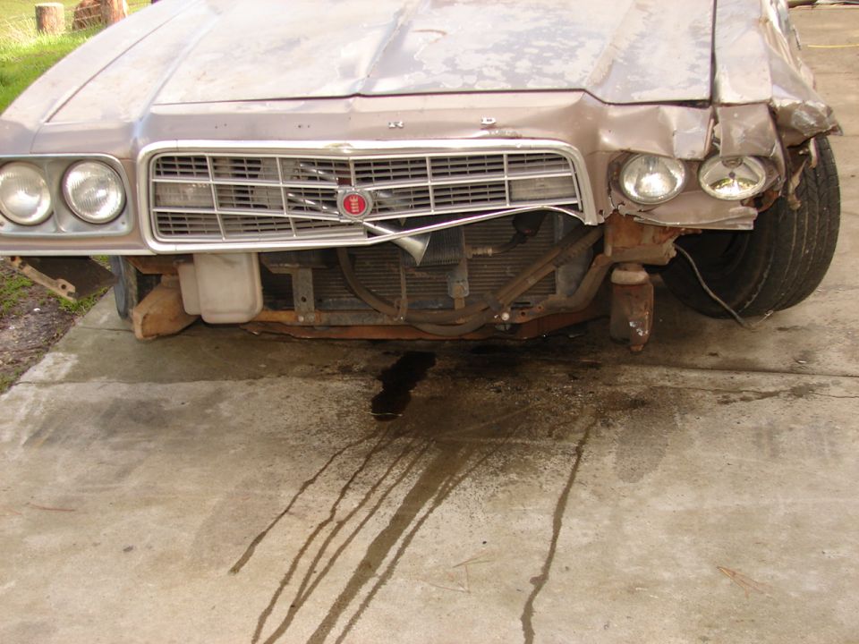 Wrecked 1970s Ford front end with bumper removed, crushed fender and fluid on driveway