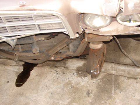 1973 Ford Ranchero - Low-angle close-up of a tan car's crumpled front end, showing torn sheet metal above the right headlight, an exposed radiator and radiator…