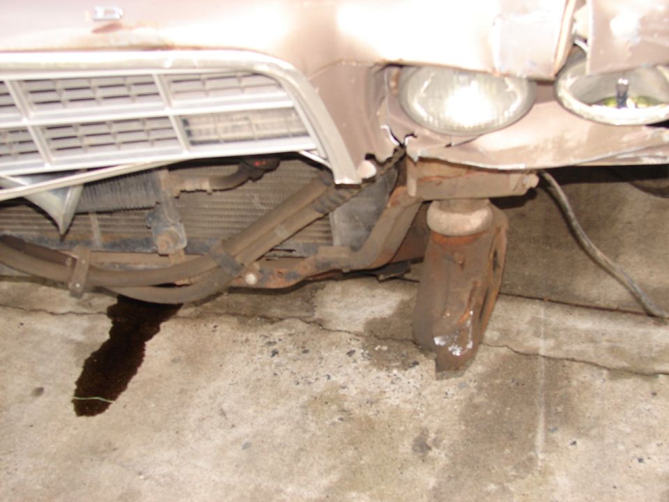 Collision damage to tan car front end with exposed radiator and bent bumper bracket