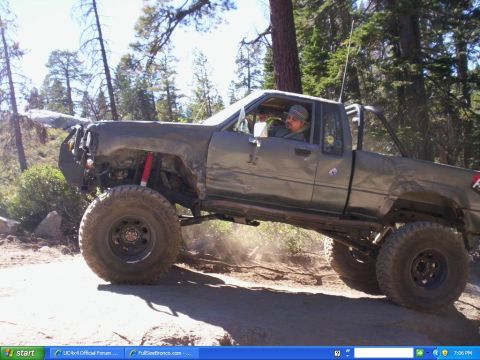 1989 Ford Bronco - A man drives a heavily modified pickup truck off-road through a wooded area.