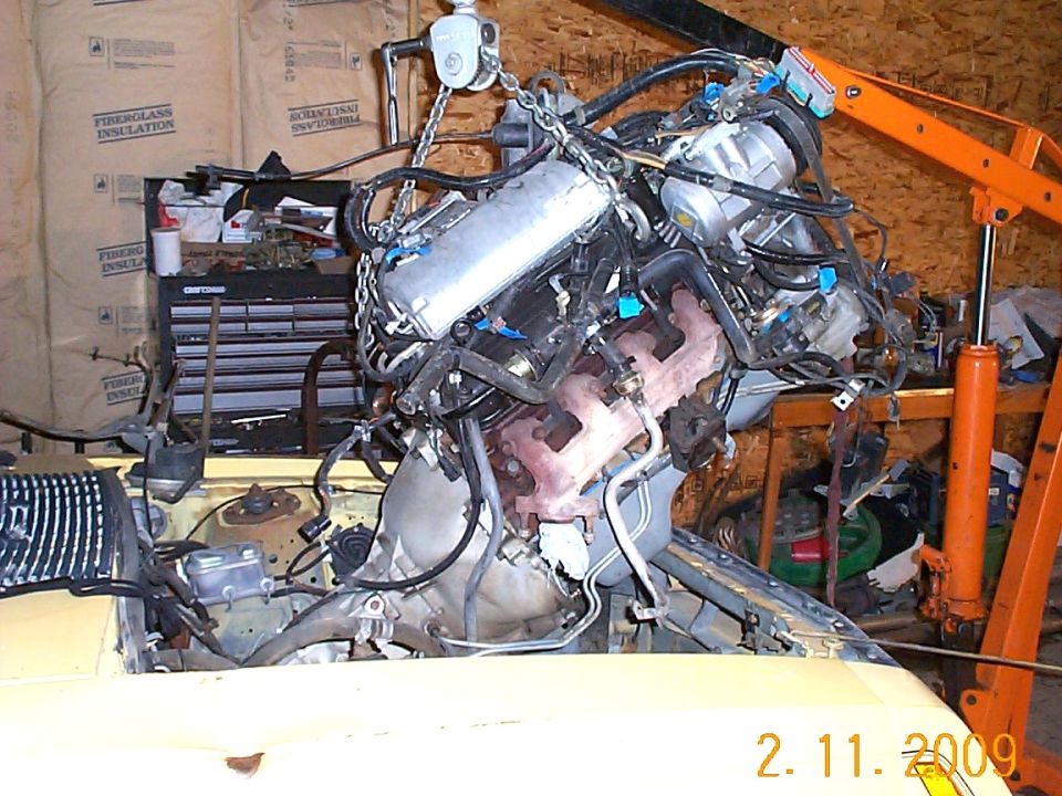 Yellow car engine bay with engine hoisted above, toolbox and insulation in background.