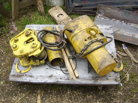 1989 Ford Bronco - Two yellow industrial hoists are resting on a wooden pallet outdoors. One hoist is a trolley with wheels, and the other is a larger cylindr…
