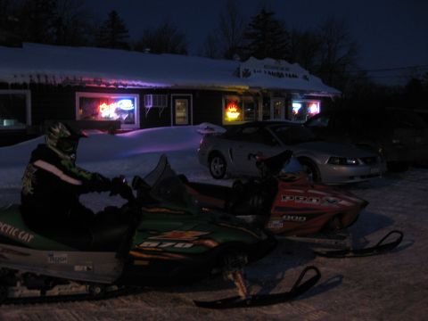 1995 Ford Bronco - Two snowmobiles are parked in the snow in front of a building with neon lights. A person wearing a helmet and snow gear is sitting on the g…