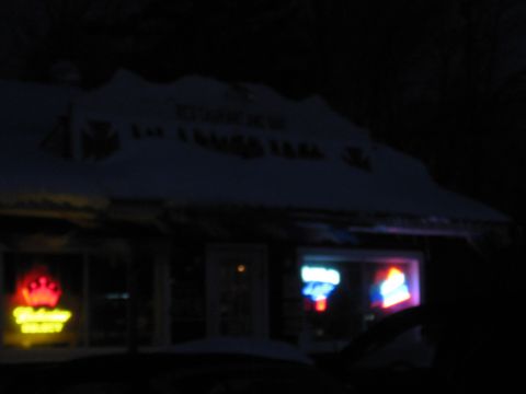 1995 Ford Bronco - A blurry nighttime photo shows the front of a building with neon signs in the windows. Snow covers the roof of the building.