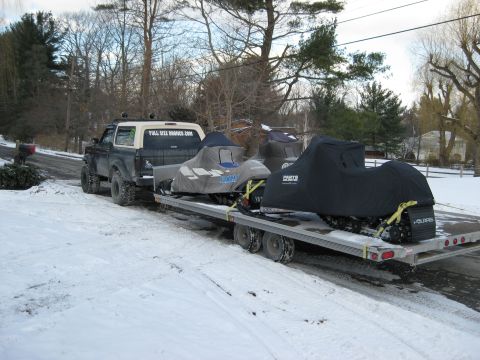 1995 Ford Bronco - A lifted, dark-colored Ford Bronco tows a trailer loaded with two snowmobiles in a snowy environment. The Bronco has a white camper shell w…