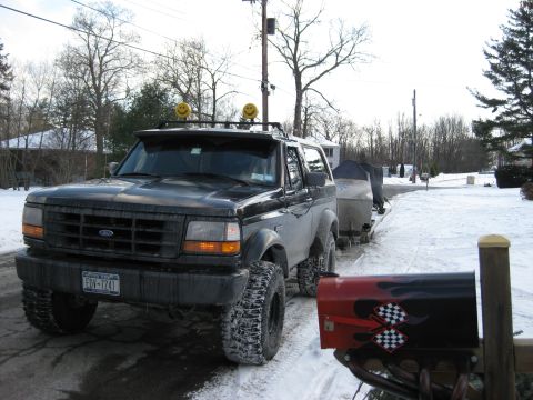 1995 Ford Bronco - A black 1995 Ford Bronco is parked in a snowy driveway next to a trailer with a boat. The truck has large off-road tires and two smiley fac…
