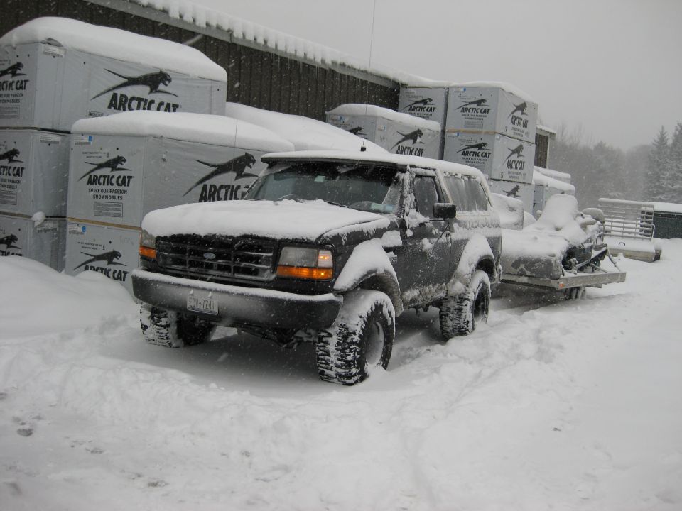 Snow-covered 1995 Ford Bronco with a snowmobile trailer in a snowy outdoor setting.