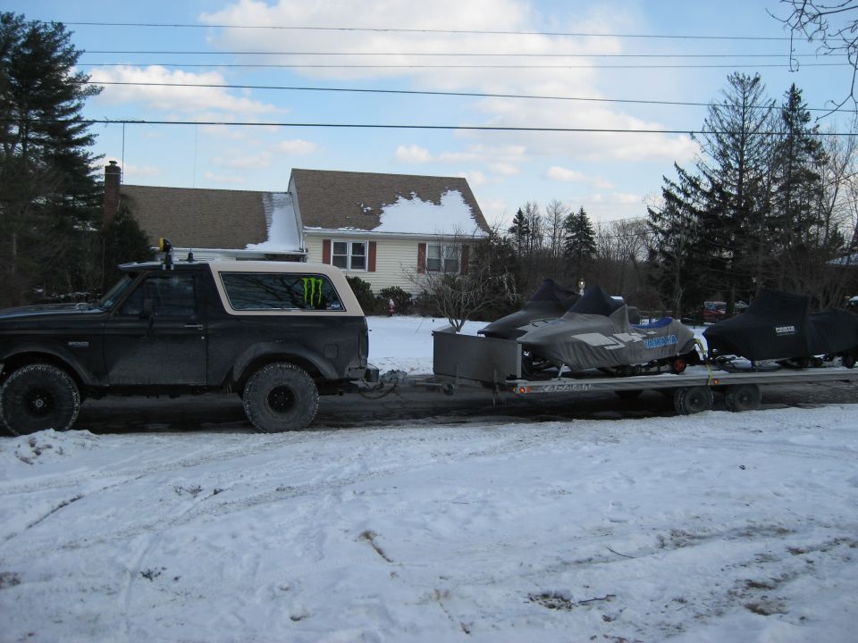 Ford Bronco towing a trailer with snowmobiles in the snow.