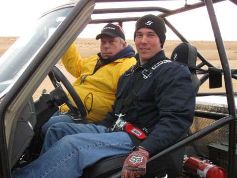 2004 Jeep Wrangler - Two men sit inside a dune buggy with a roll cage, wearing racing harnesses and helmets. The man on the left wears a yellow jacket and a bla…