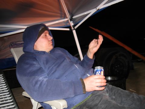 2004 Jeep Wrangler - A person wearing a blue hoodie and beanie sits in a chair holding a can of soda and a phone. The person is sitting under a canopy at night.