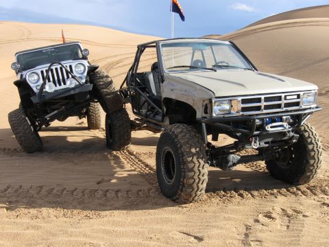 2004 Jeep Wrangler - Two off-road vehicles are parked on sand dunes under a blue sky. The vehicle in the foreground is a tan Toyota pickup truck with a roll cag…