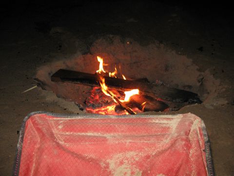 2004 Jeep Wrangler - A campfire burns in a sandy pit at night, with a red camping chair in the foreground.