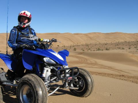 2004 Jeep Wrangler - A person in a blue riding suit and white helmet sits on a blue ATV in a desert landscape with sand dunes under a clear blue sky.