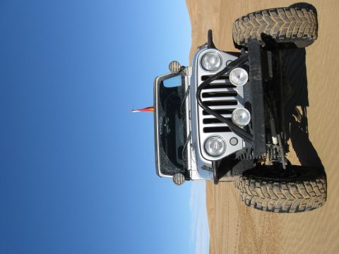 2004 Jeep Wrangler - A silver Jeep Wrangler with off-road tires and a brush guard is parked on a sand dune under a clear blue sky. A small flag with red, yellow…