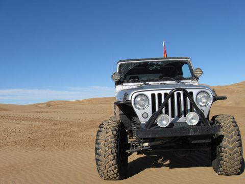 2004 Jeep Wrangler - A silver Jeep Wrangler is parked on a sandy dune under a clear blue sky. The front of the vehicle is angled towards the camera, showing its…