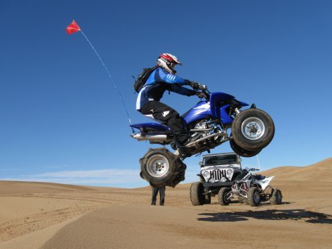 2004 Jeep Wrangler - A blue quad bike is airborne over a white Jeep Wrangler and a white quad bike in a desert landscape. The rider on the airborne quad is wear…
