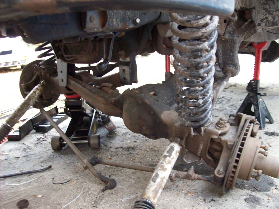 Underside of a lifted 1986 Ford Bronco showing front suspension, coil spring, shock, and jack stands.