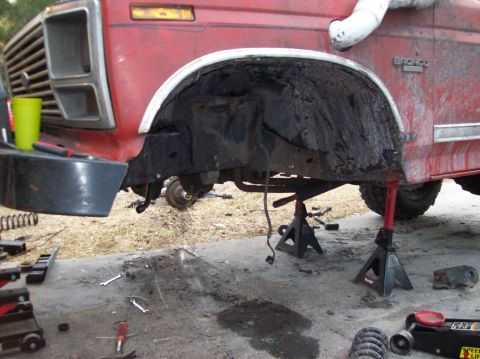 1986 Ford Bronco - The front fender well of a red Ford Bronco is shown with the wheel removed and the vehicle supported by jack stands. Tools and parts are sc…