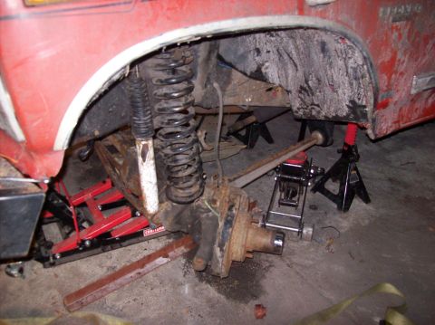 1986 Ford Bronco - The undercarriage of a red vehicle, likely a 1986 Ford Bronco, is shown with the suspension components exposed and supported by jack stands…