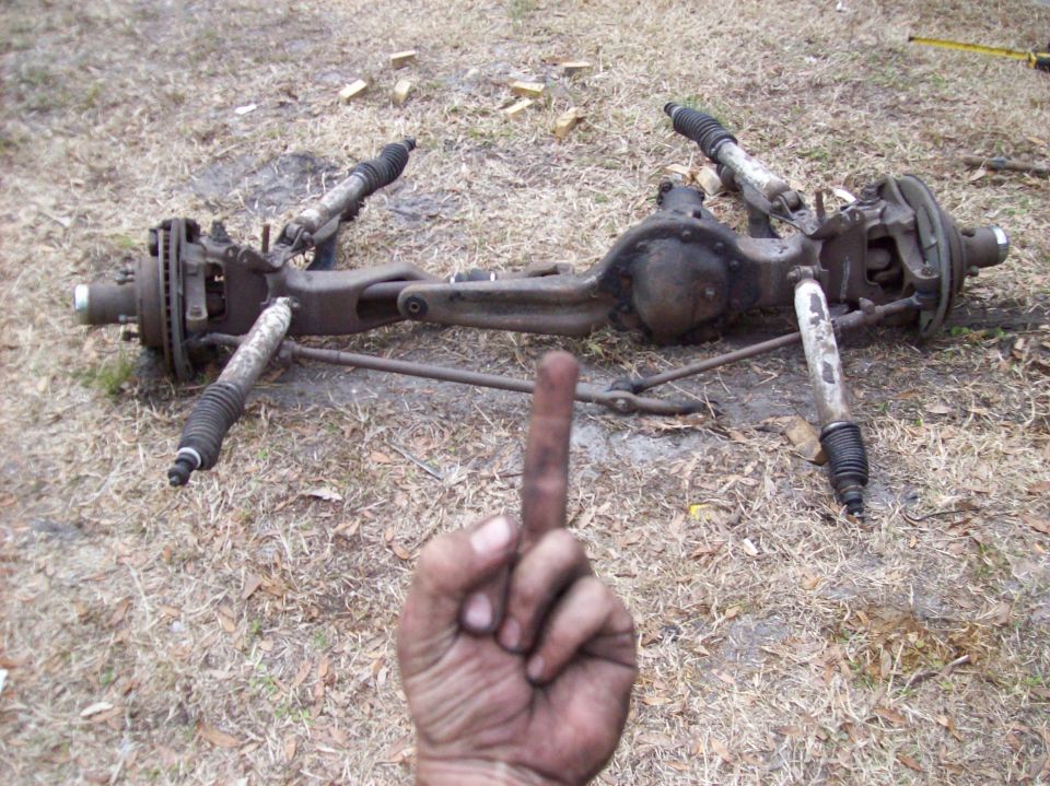Disassembled vehicle front axle assembly on the ground with a hand giving the middle finger.
