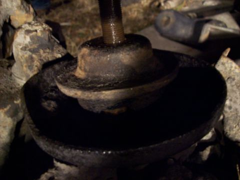 1986 Ford Bronco - A close-up, low-angle shot shows a rusty metal suspension component, likely a spring perch or mount, with a threaded bolt extending upwards…