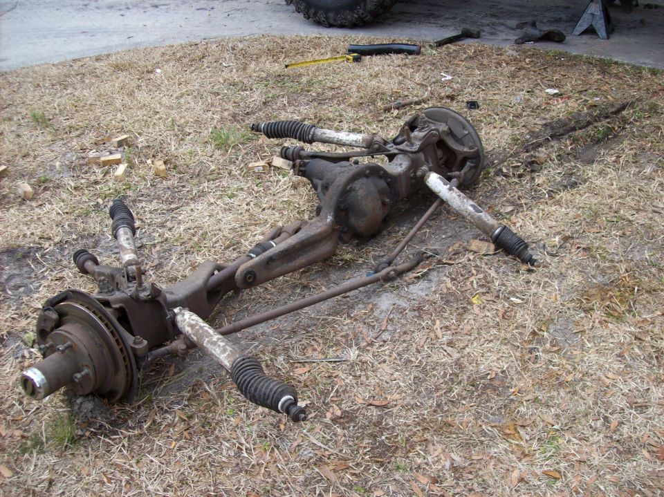 Disassembled 1986 Ford Bronco front axle assembly on dry grass.