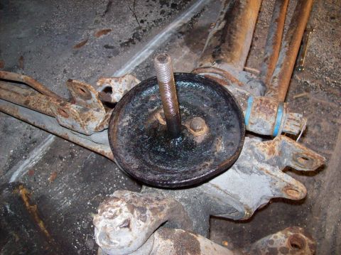 1986 Ford Bronco - A close-up view of heavily rusted suspension components, including a brake drum and a threaded bolt, likely from the rear axle of a vehicle.