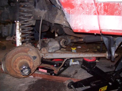 1986 Ford Bronco - The underside of a red vehicle, likely a Ford Bronco, is shown with suspension components and a differential visible. The vehicle is suppor…